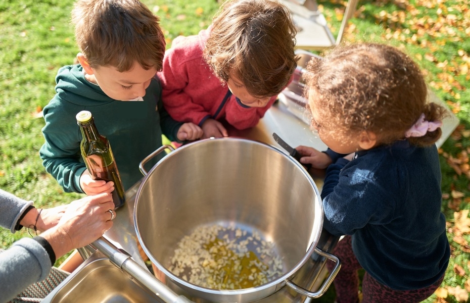 Drei Kinder gucken von oben in einen Kochtopf.