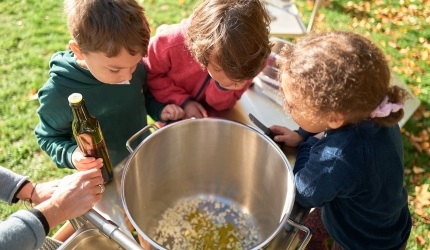 Drei Kinder gucken von oben in einen Kochtopf.