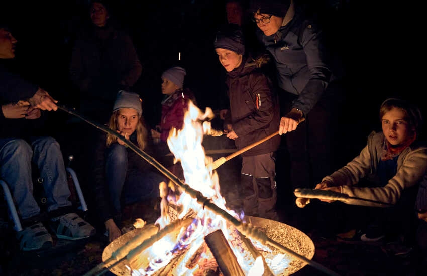 Stockbrot zubereitende Personen, in der Mitte eine Feuerschale 