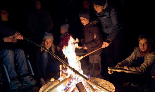 Stockbrot zubereitende Personen, in der Mitte eine Feuerschale 
