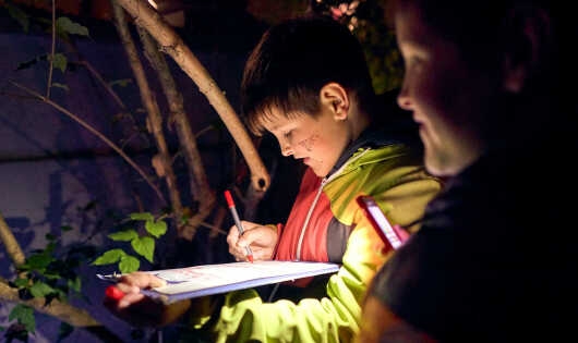 Von Taschenlampe angeleuchteter Junge schreibt etwas auf einem Klemmbrett