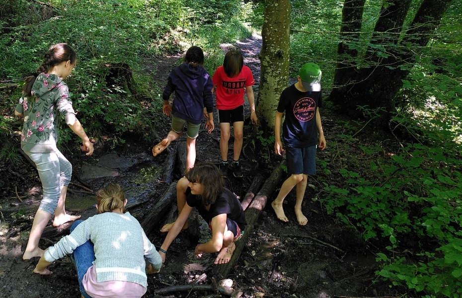 Sechs Kinder forschend auf matschigem Waldweg